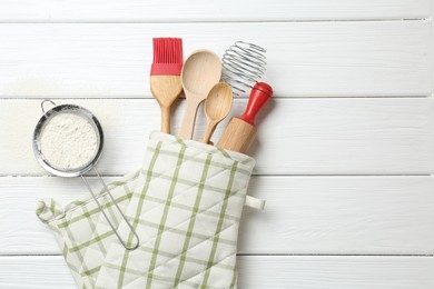 Photo of Different kitchen utensils in oven mitten and flour on white wooden table, flat lay. Space for text