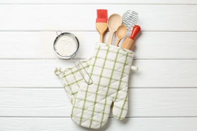 Photo of Different kitchen utensils in oven mitten and flour on white wooden table, flat lay