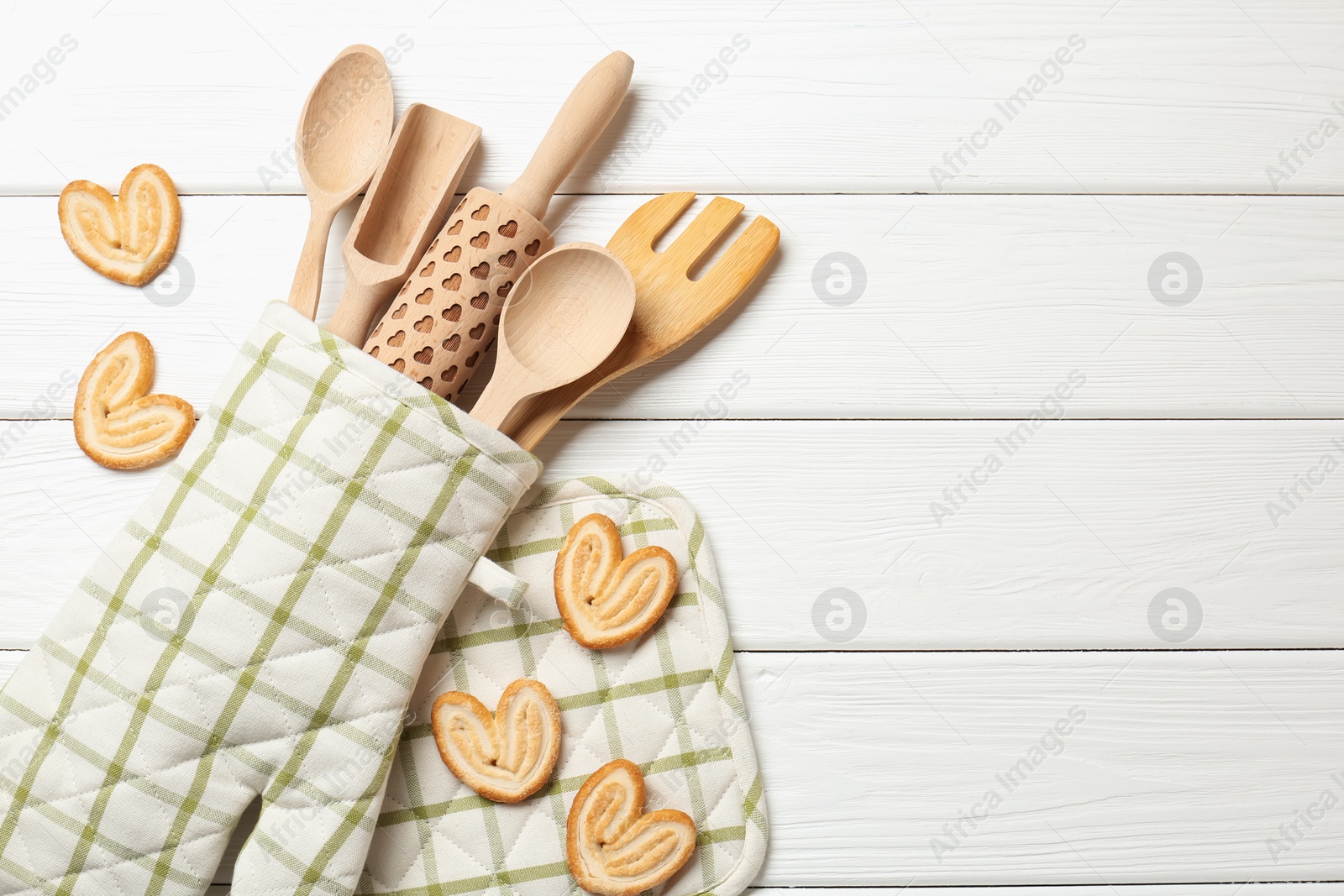 Different kitchen utensils in oven mitten and palmier cookies on white wooden table, flat lay. Space for text Photo of Different kitchen utensils in oven mitten and palmier cookies on white wooden table, flat lay. Space for text