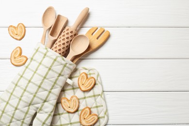 Photo of Different kitchen utensils in oven mitten and palmier cookies on white wooden table, flat lay. Space for text