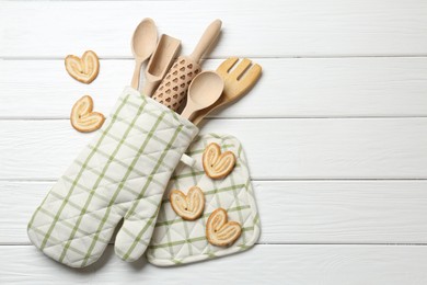 Photo of Different kitchen utensils in oven mitten and palmier cookies on white wooden table, flat lay. Space for text