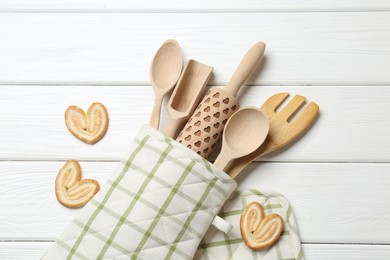 Photo of Different kitchen utensils in oven mitten and palmier cookies on white wooden table, flat lay