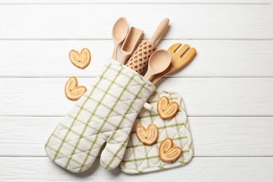 Photo of Different kitchen utensils in oven mitten and palmier cookies on white wooden table, flat lay