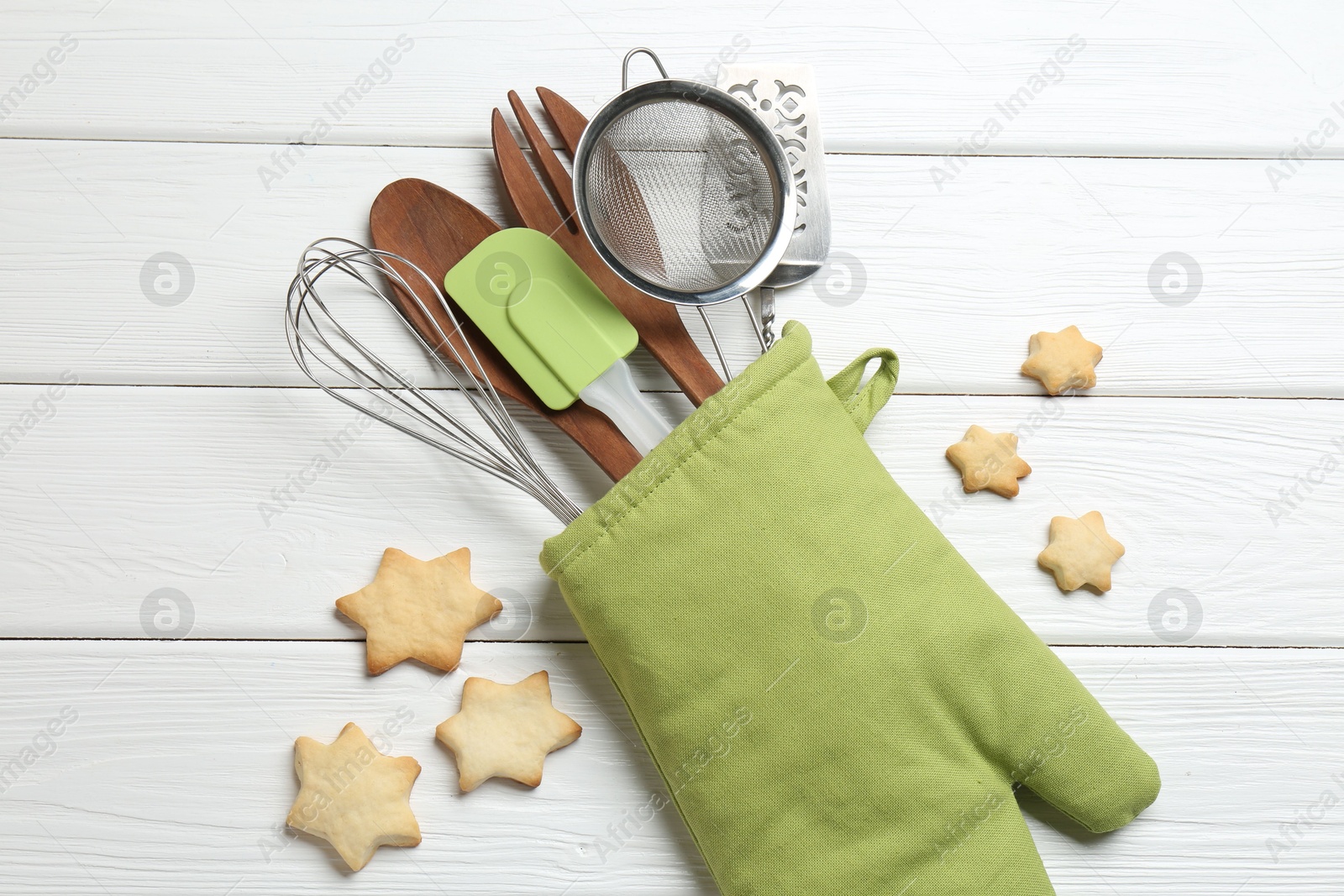 Different kitchen utensils in oven mitten and star shaped cookies on white wooden table, flat lay Photo of Different kitchen utensils in oven mitten and star shaped cookies on white wooden table, flat lay