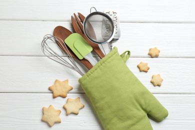 Photo of Different kitchen utensils in oven mitten and star shaped cookies on white wooden table, flat lay