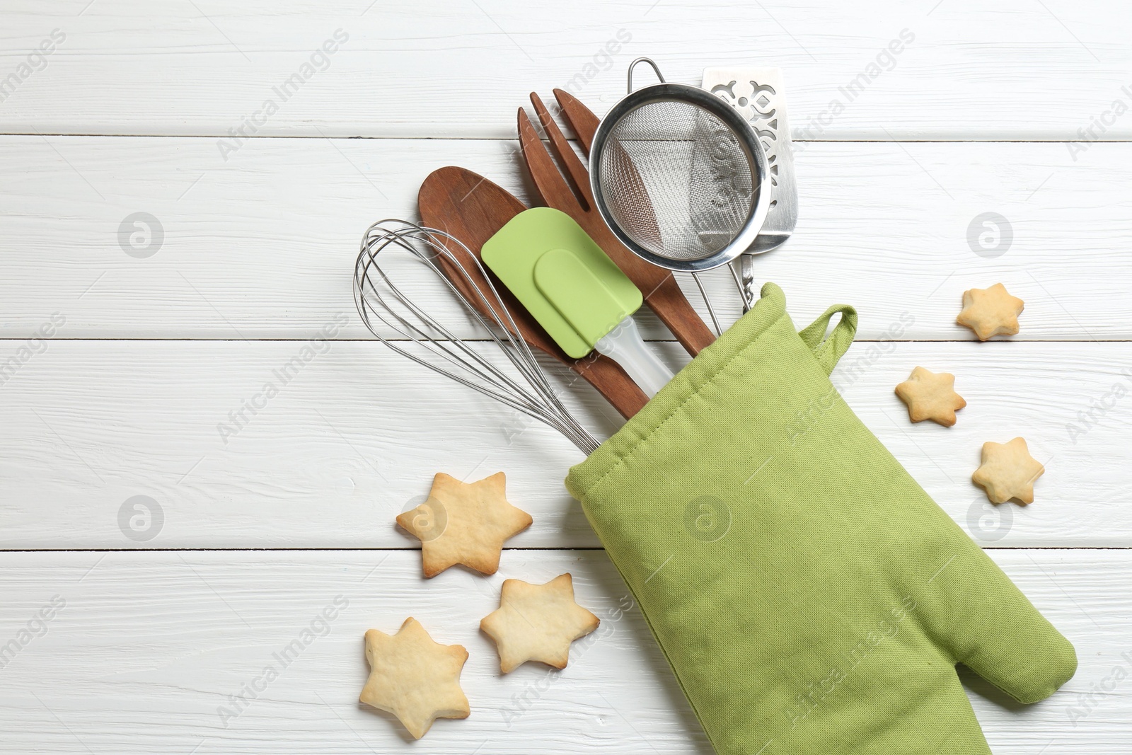 Different kitchen utensils in oven mitten and star shaped cookies on white wooden table, flat lay. Space for text Photo of Different kitchen utensils in oven mitten and star shaped cookies on white wooden table, flat lay. Space for text