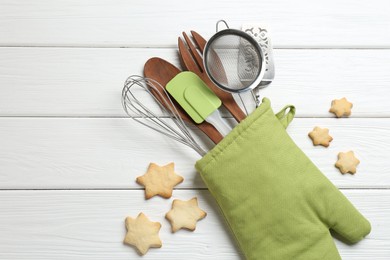Photo of Different kitchen utensils in oven mitten and star shaped cookies on white wooden table, flat lay. Space for text
