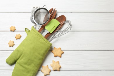 Photo of Different kitchen utensils in oven mitten and star shaped cookies on white wooden table, flat lay. Space for text