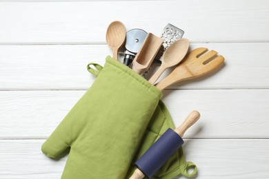 Photo of Different kitchen utensils in oven mitten on white wooden table, top view