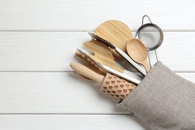 Photo of Different kitchen utensils in oven mitten on white wooden table, top view. Space for text