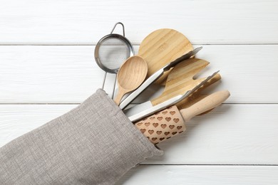 Photo of Different kitchen utensils in oven mitten on white wooden table, top view
