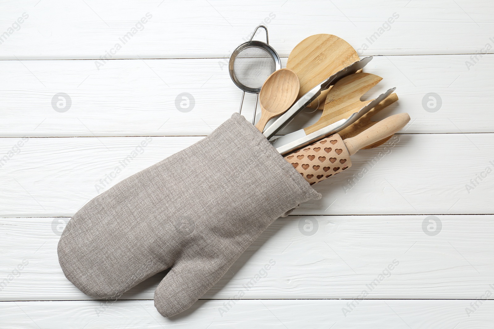 Different kitchen utensils in oven mitten on white wooden table, top view Photo of Different kitchen utensils in oven mitten on white wooden table, top view