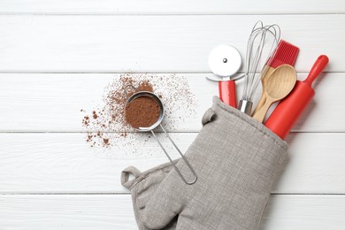 Photo of Different kitchen utensils in oven mitten and cinnamon on white wooden table, flat lay. Space for text