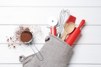 Photo of Different kitchen utensils in oven mitten and cinnamon on white wooden table, flat lay