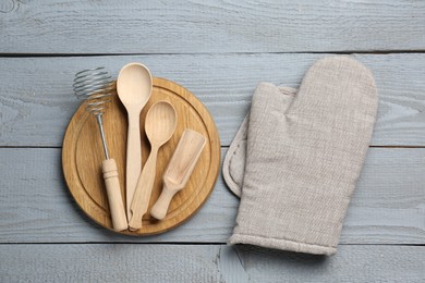 Photo of Different kitchen utensils and oven mitten on light grey wooden table, flat lay