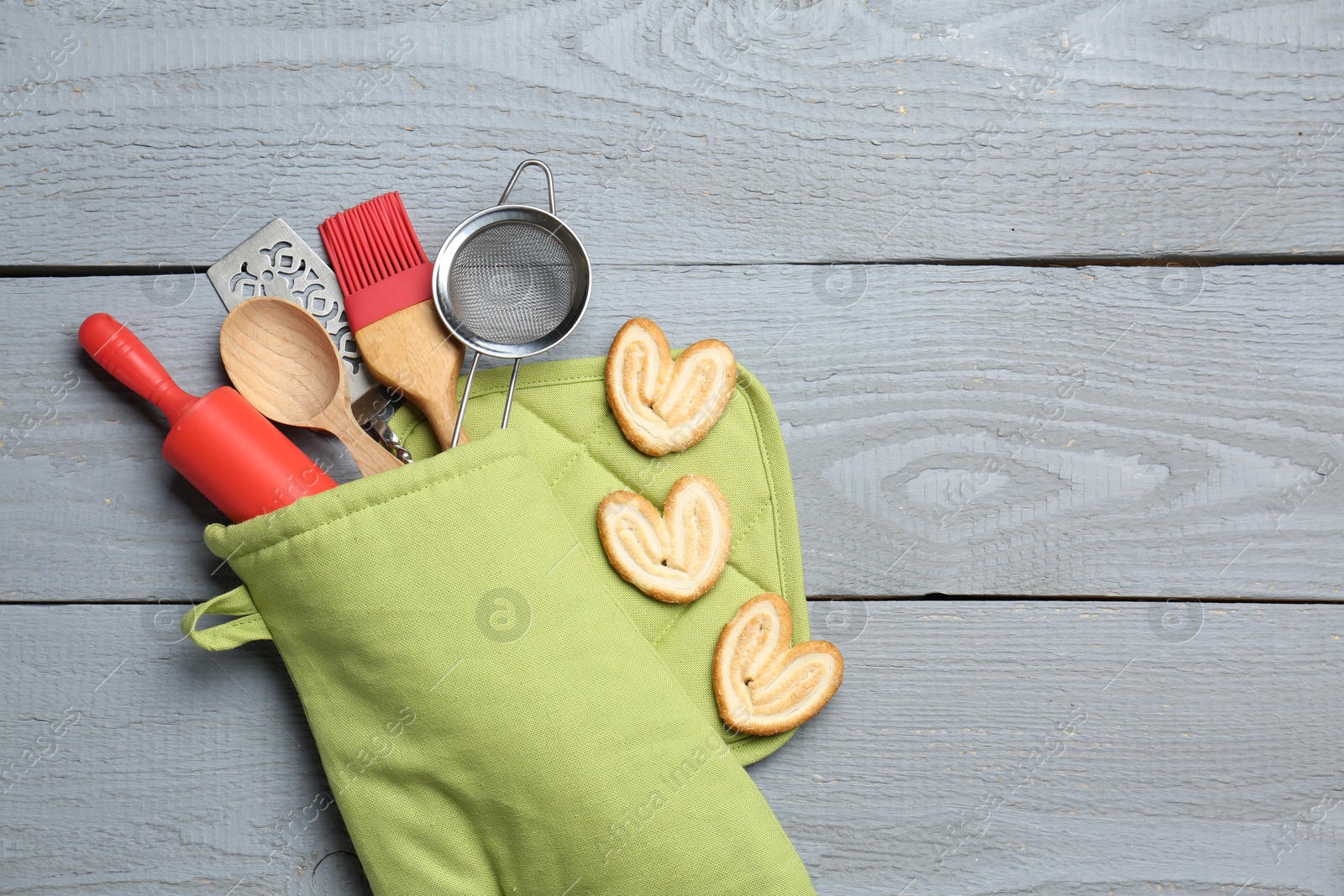Different kitchen utensils in oven mitten and palmier cookies on light grey wooden table, flat lay. Space for text Photo of Different kitchen utensils in oven mitten and palmier cookies on light grey wooden table, flat lay. Space for text