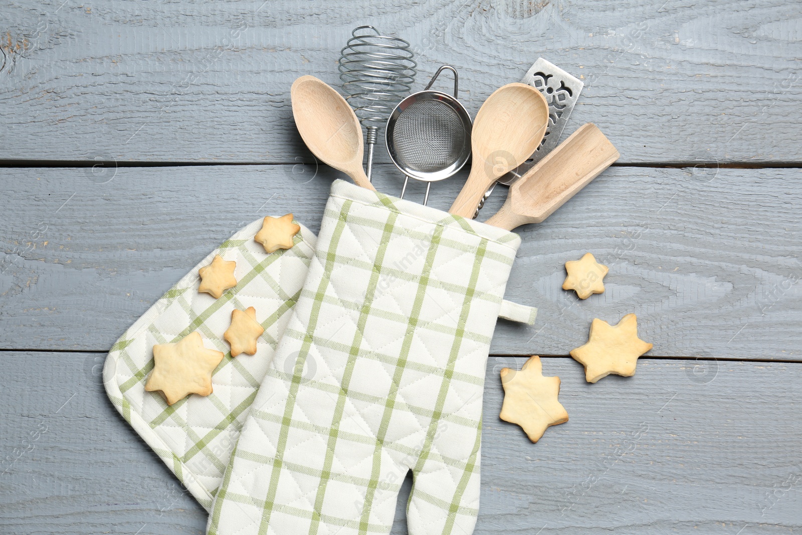 Different kitchen utensils in oven mitten and star shaped cookies on light grey wooden table, flat lay Photo of Different kitchen utensils in oven mitten and star shaped cookies on light grey wooden table, flat lay