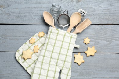 Photo of Different kitchen utensils in oven mitten and star shaped cookies on light grey wooden table, flat lay