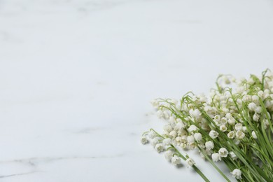 Photo of Beautiful lily-of-the-valley flowers on white marble background, closeup. Space for text