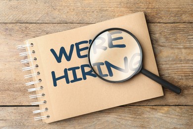 Image of We Are Hiring. Notebook with magnifying glass on wooden table, top view. Recruitment, human resources concept