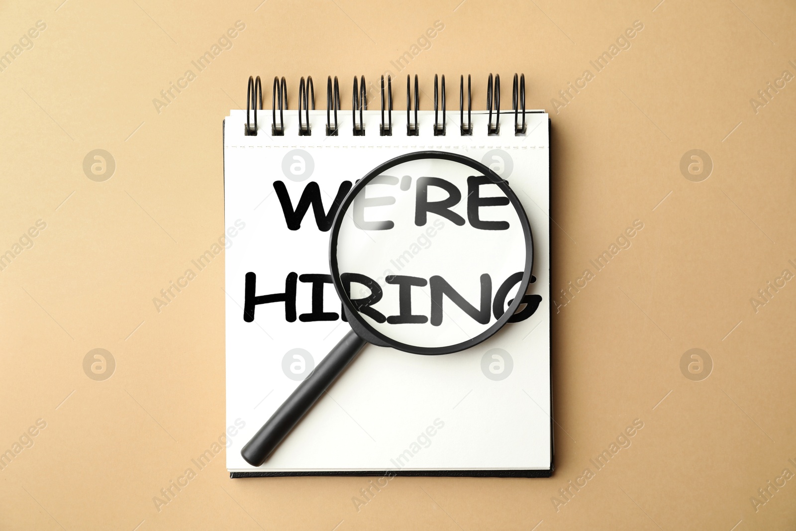 We Are Hiring. Notebook with magnifying glass on beige background, top view. Recruitment, human resources concept Image of We Are Hiring. Notebook with magnifying glass on beige background, top view. Recruitment, human resources concept