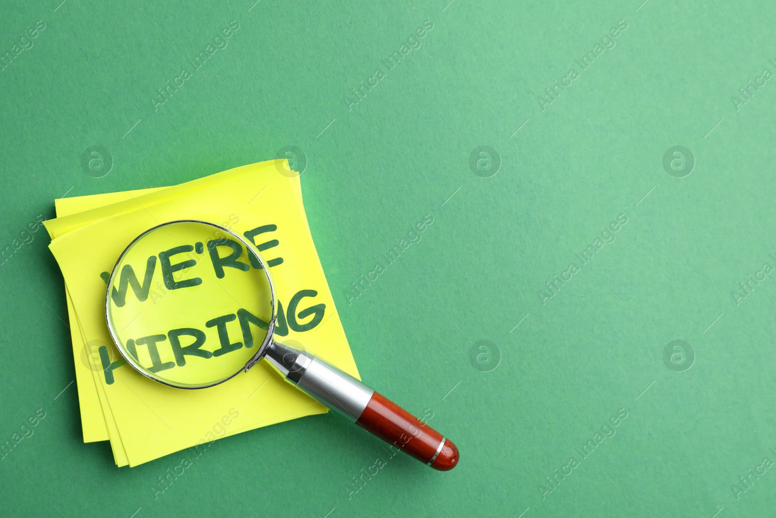 We Are Hiring. Paper notes with magnifying glass on green background, top view. Recruitment, human resources concept Image of We Are Hiring. Paper notes with magnifying glass on green background, top view. Recruitment, human resources concept
