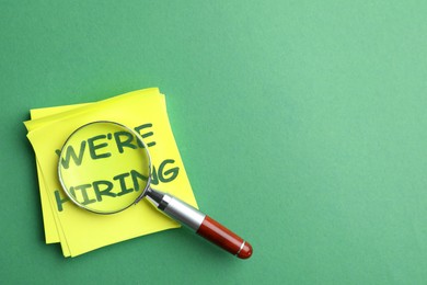 Image of We Are Hiring. Paper notes with magnifying glass on green background, top view. Recruitment, human resources concept