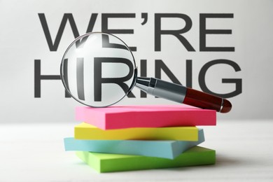 Image of We Are Hiring. Paper notes and magnifying glass on white table. Recruitment, human resources concept