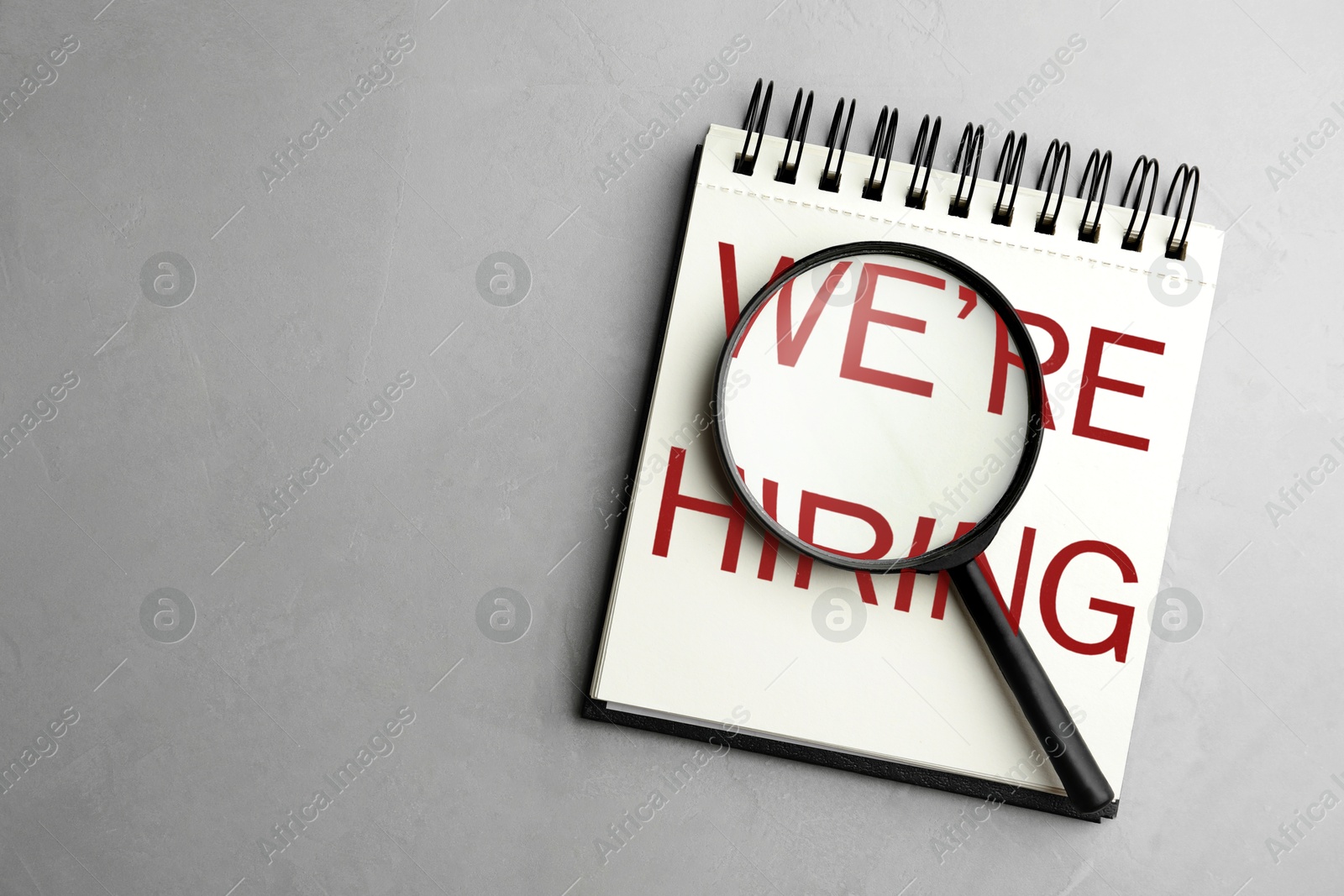 We Are Hiring. Notebook and magnifying glass on grey background, top view. Recruitment, human resources concept Image of We Are Hiring. Notebook and magnifying glass on grey background, top view. Recruitment, human resources concept