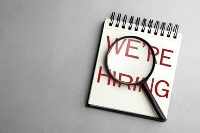 Image of We Are Hiring. Notebook and magnifying glass on grey background, top view. Recruitment, human resources concept