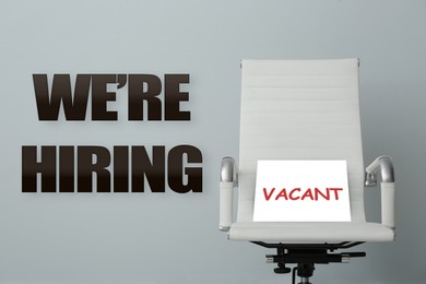 Image of We Are Hiring. Office chair with Vacant sign on grey background. Recruitment, human resources concept