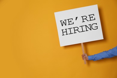 Image of Man holding sign with phrase We Are Hiring on yellow background, closeup. Recruitment, human resources concept
