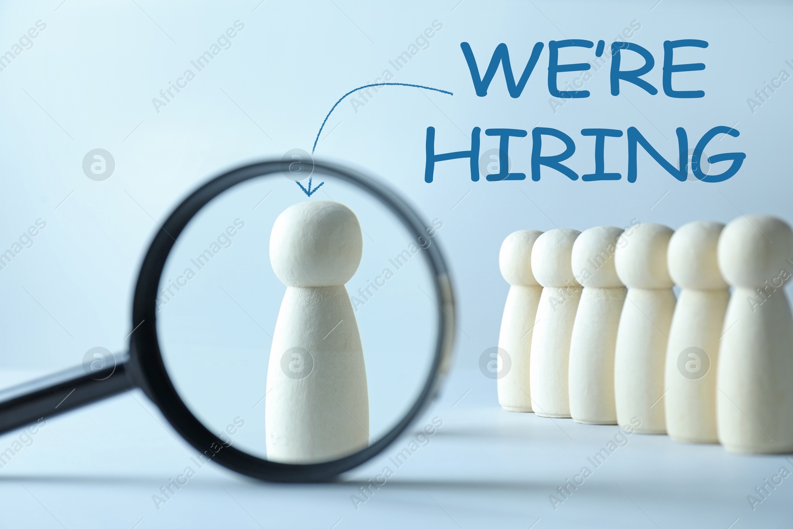 We Are Hiring. Wooden figure standing apart among others on light blue background, view through magnifying glass. Recruitment, human resources concept Image of We Are Hiring. Wooden figure standing apart among others on light blue background, view through magnifying glass. Recruitment, human resources concept
