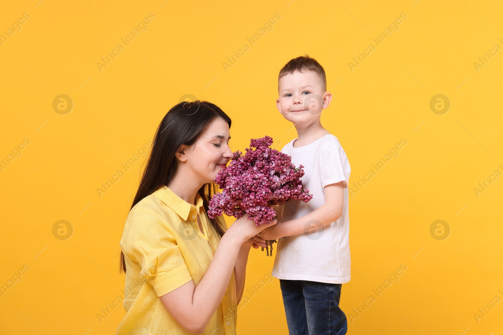 Photo of Mother and her son with bouquet of lilac flowers on yellow background