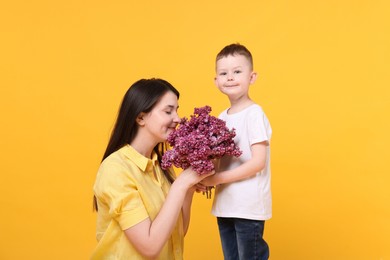 Photo of Mother and her son with bouquet of lilac flowers on yellow background