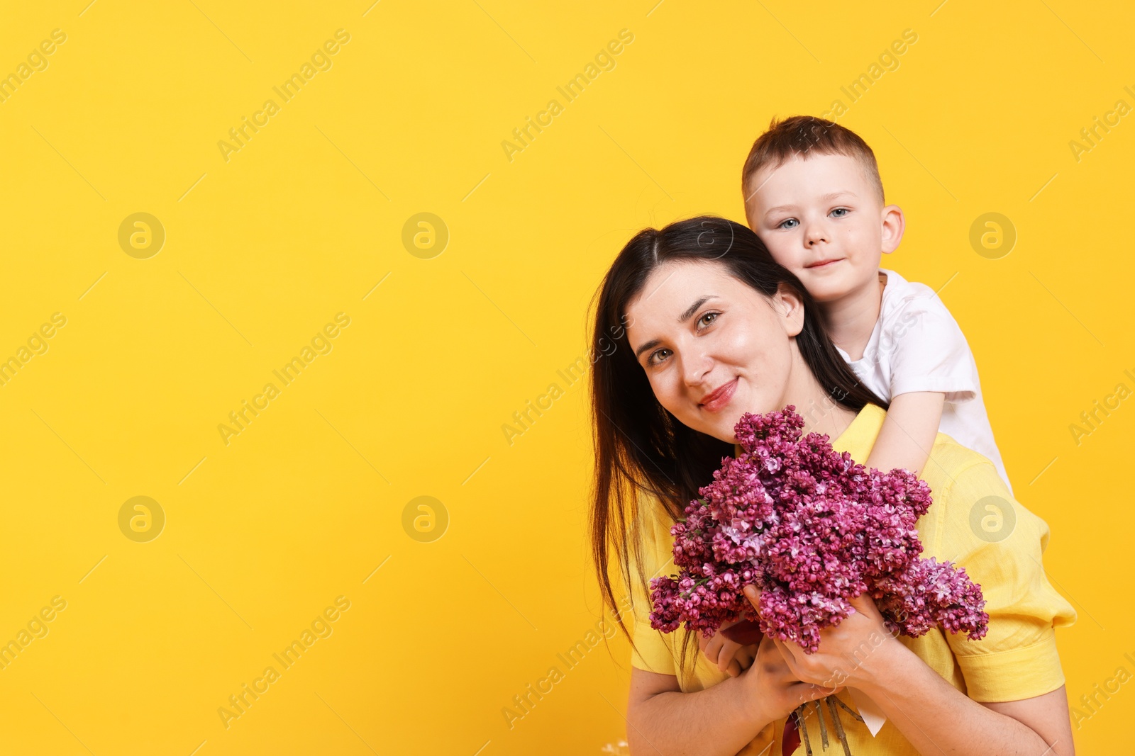 Photo of Mother and her son with bouquet of lilac flowers on yellow background, space for text
