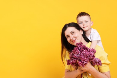 Photo of Mother and her son with bouquet of lilac flowers on yellow background, space for text