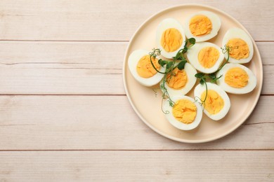 Photo of Boiled eggs and microgreens on wooden table, top view. Space for text