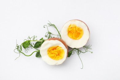Photo of Halves of hard boiled egg and microgreens on white background, top view