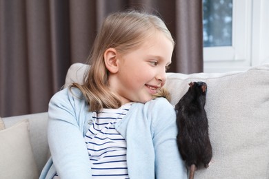 Photo of Little girl with cute black rat on sofa at home