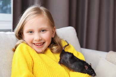 Photo of Little girl with cute black rat on sofa at home