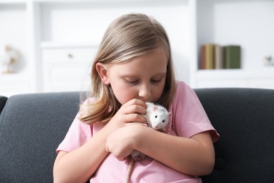 Photo of Little girl with cute white rat on sofa at home