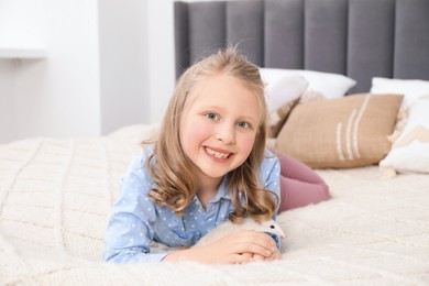 Photo of Little girl with cute white rat on bed at home