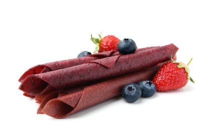 Photo of Tasty fruit leather rolls, strawberries and blueberries isolated on white