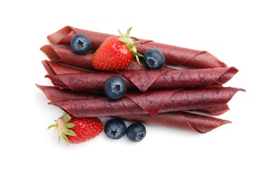 Photo of Tasty fruit leather rolls, strawberries and blueberries isolated on white, top view