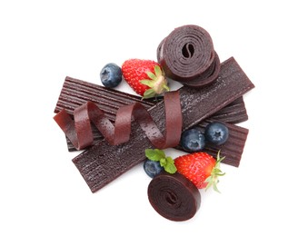 Photo of Tasty fruit leather rolls, strawberries and blueberries isolated on white, top view