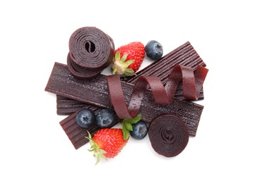 Photo of Tasty fruit leather rolls, strawberries and blueberries isolated on white, top view