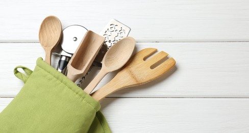 Photo of Different kitchen utensils in oven mitten on white wooden table, top view. Space for text