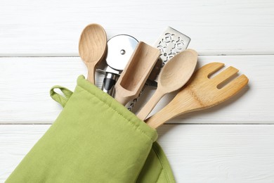 Photo of Different kitchen utensils in oven mitten on white wooden table, top view
