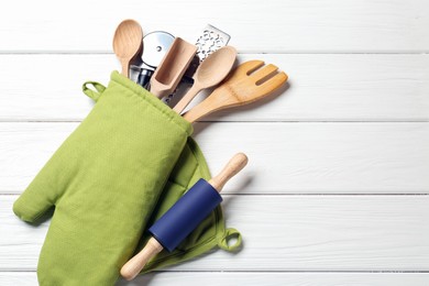 Photo of Different kitchen utensils in oven mitten on white wooden table, top view. Space for text